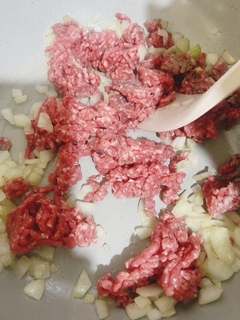 Minced beef cooking in a pan with sautéed onions, spices, and spring onions.