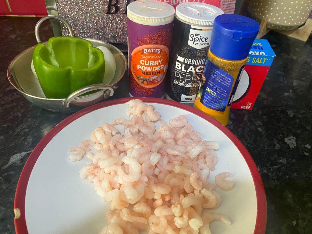 Chopped prawns on a plate with spices and a green bell pepper in the background.