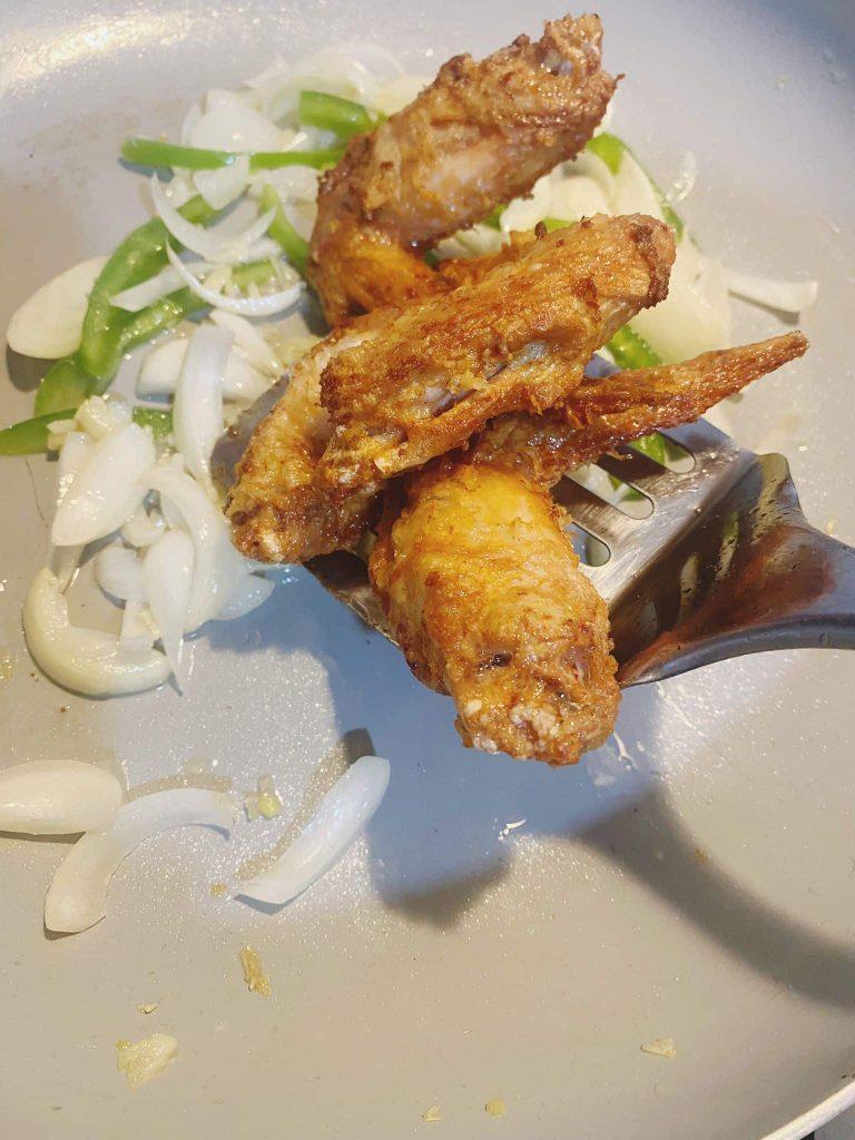 Crispy fried chicken wings added to a pan with sautéed garlic, onion, and paprika.