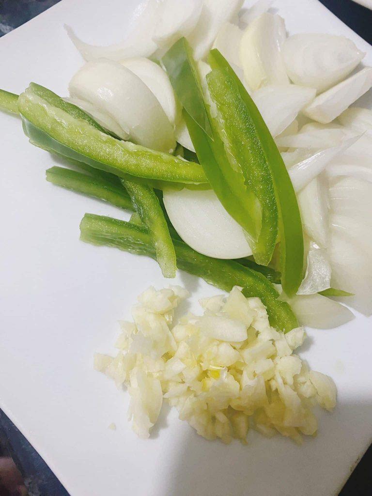 Freshly chopped garlic, onions, and green bell pepper on a white cutting board.