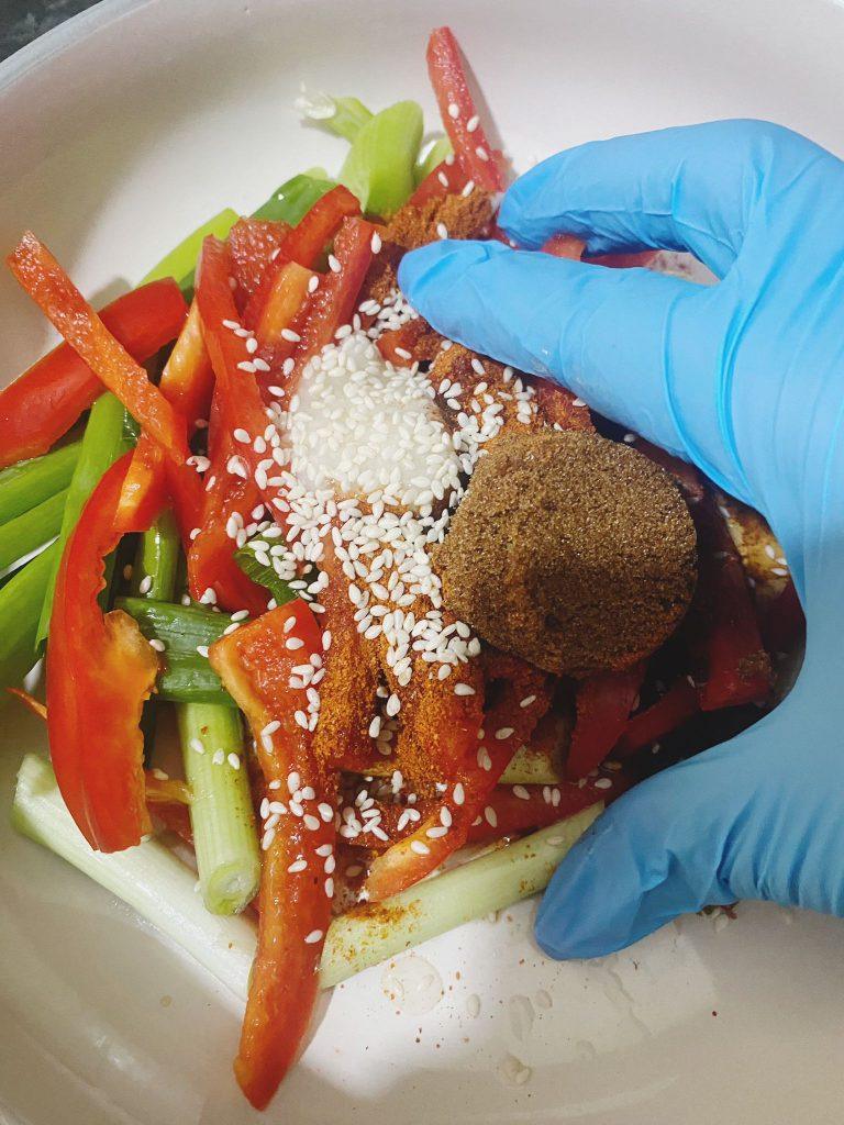 Chopped red peppers and spring onions topped with sesame seeds, brown sugar, and spices in a bowl.
