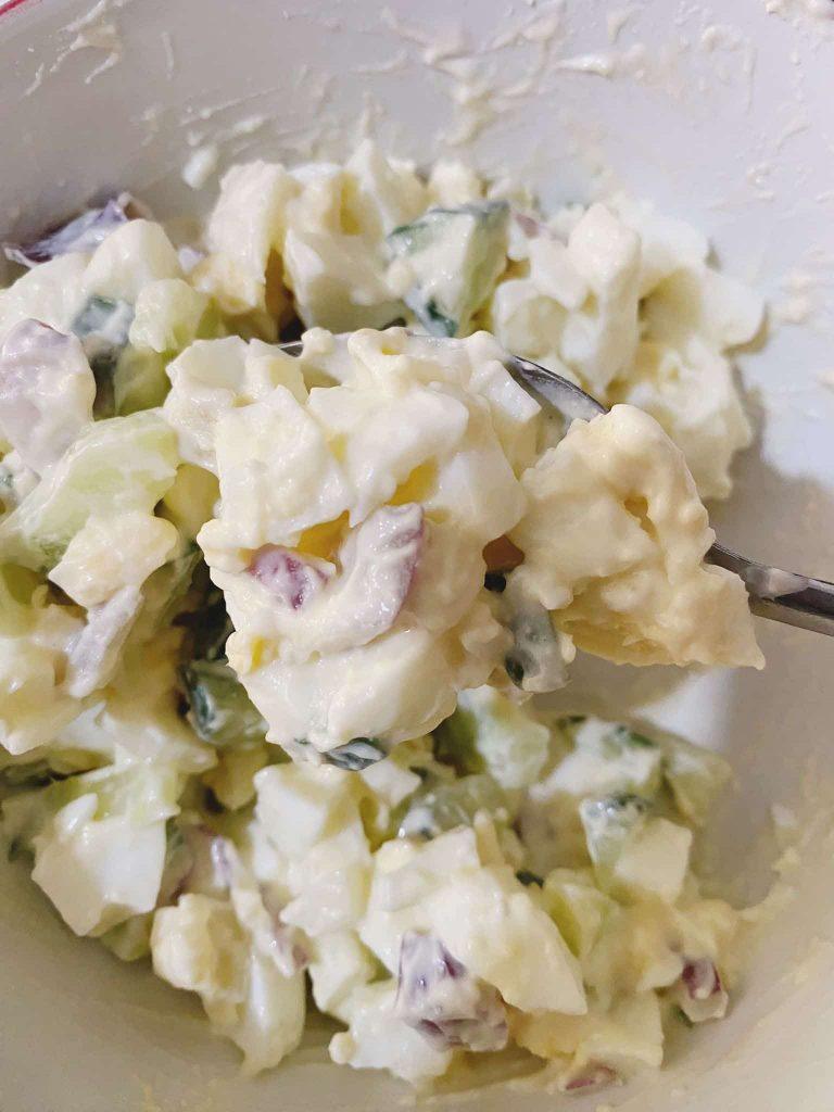 Creamy egg salad mixture with cucumber, onion, and mayonnaise in a bowl