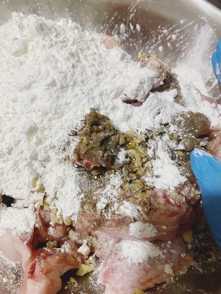  Chicken wings being coated with garlic, spices, and cornflour for marination.