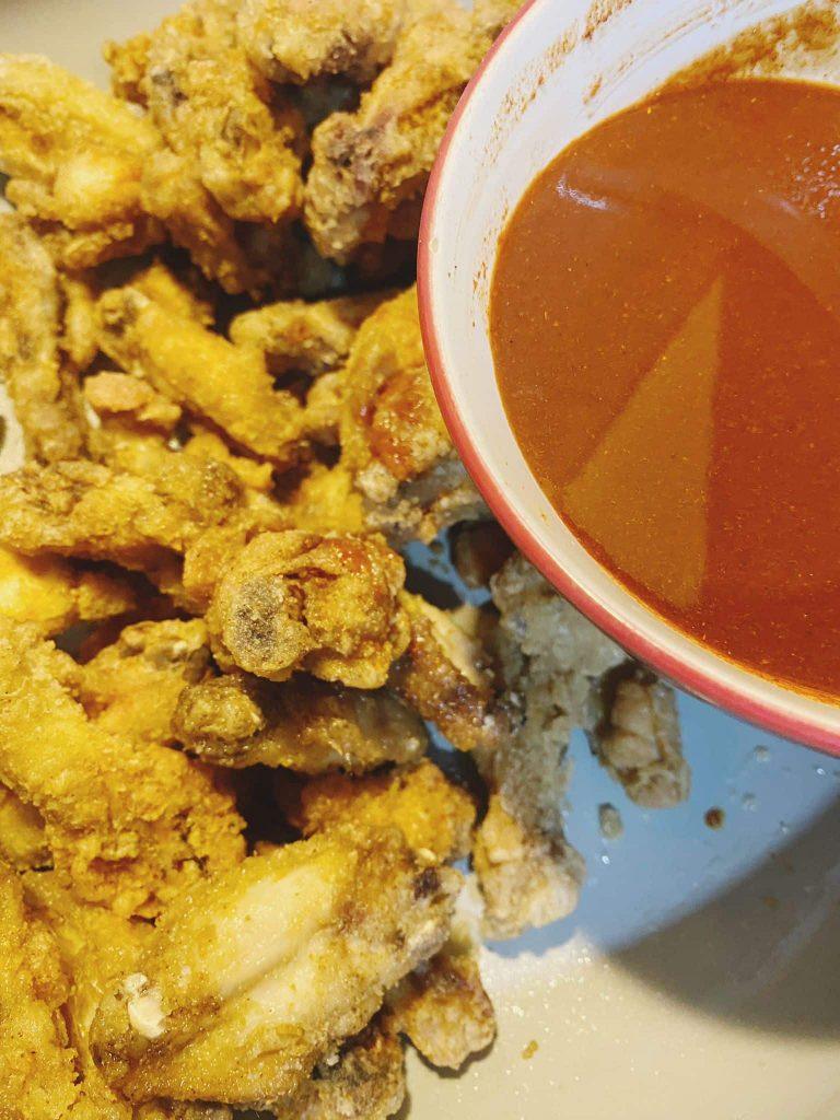 Fried chicken wings with a bowl of sauce, ready to be tossed together.