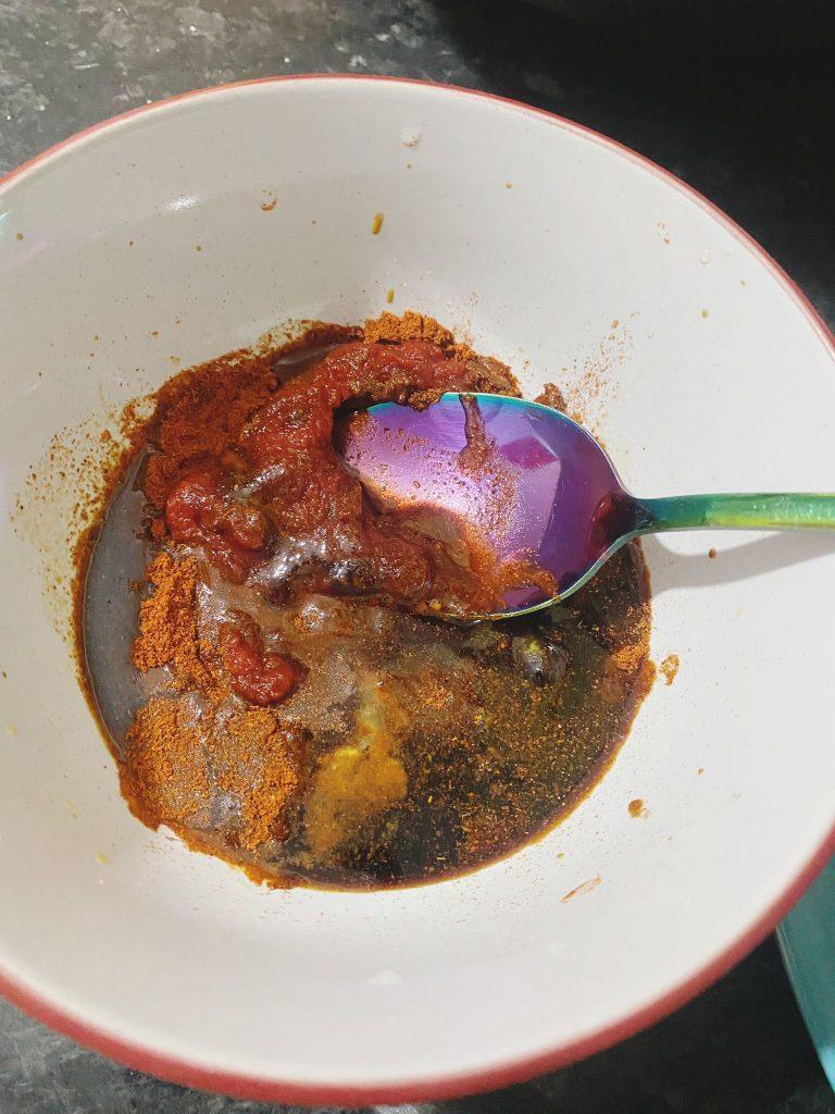 Bowl with soy sauce, tomato paste, and spices being mixed into a rich sauce.