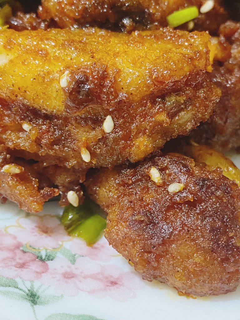 Crispy saucy chicken wings garnished with sesame seeds and spring onion.