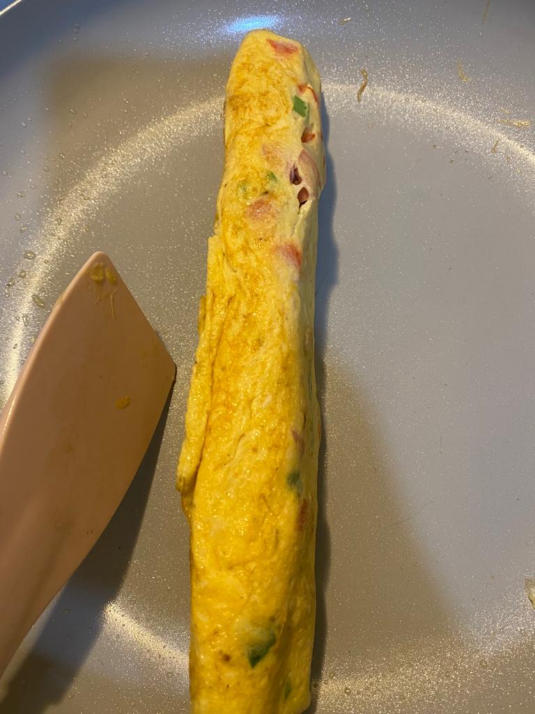Egg mixture cooking in a non-stick skillet, being gently rolled with a spatula to create a layered omelet filled with sausage and paprika