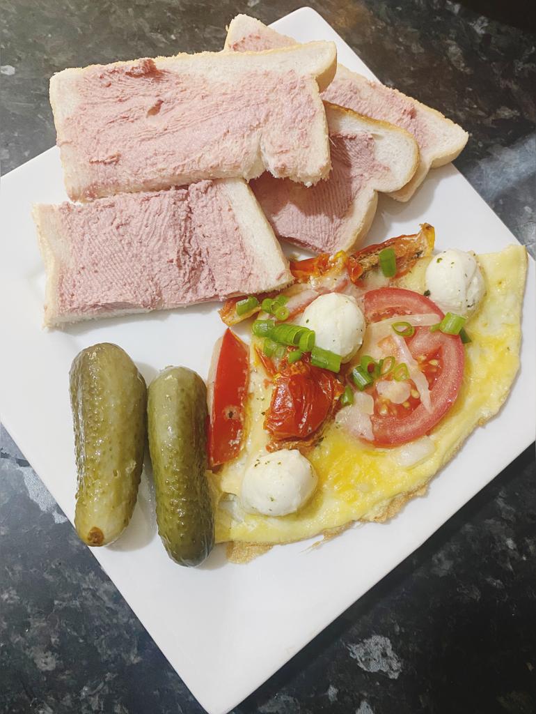 Cheesy tomato omelette served with pâté on white bread and two pickles on a white plate.