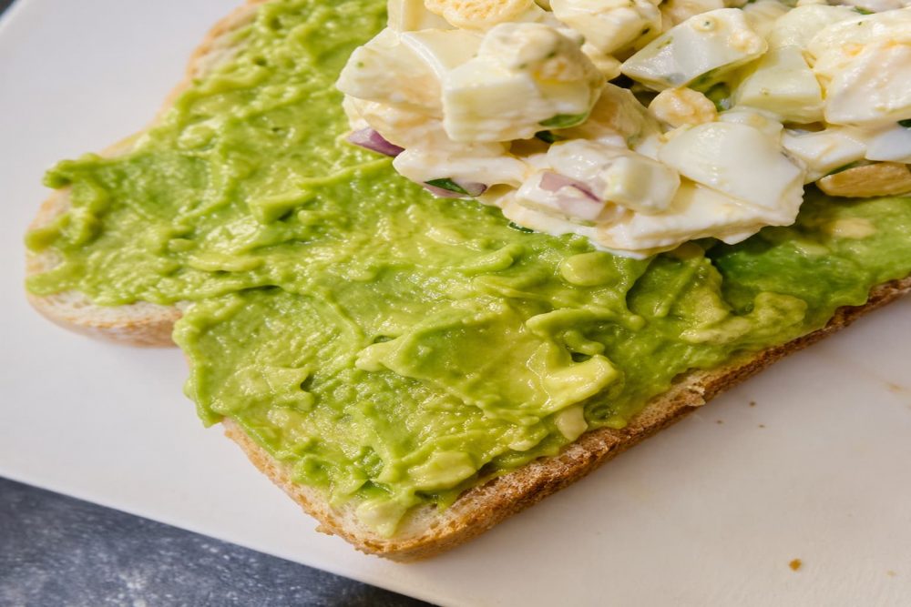 Adding egg and cucumber mixture onto avocado toast