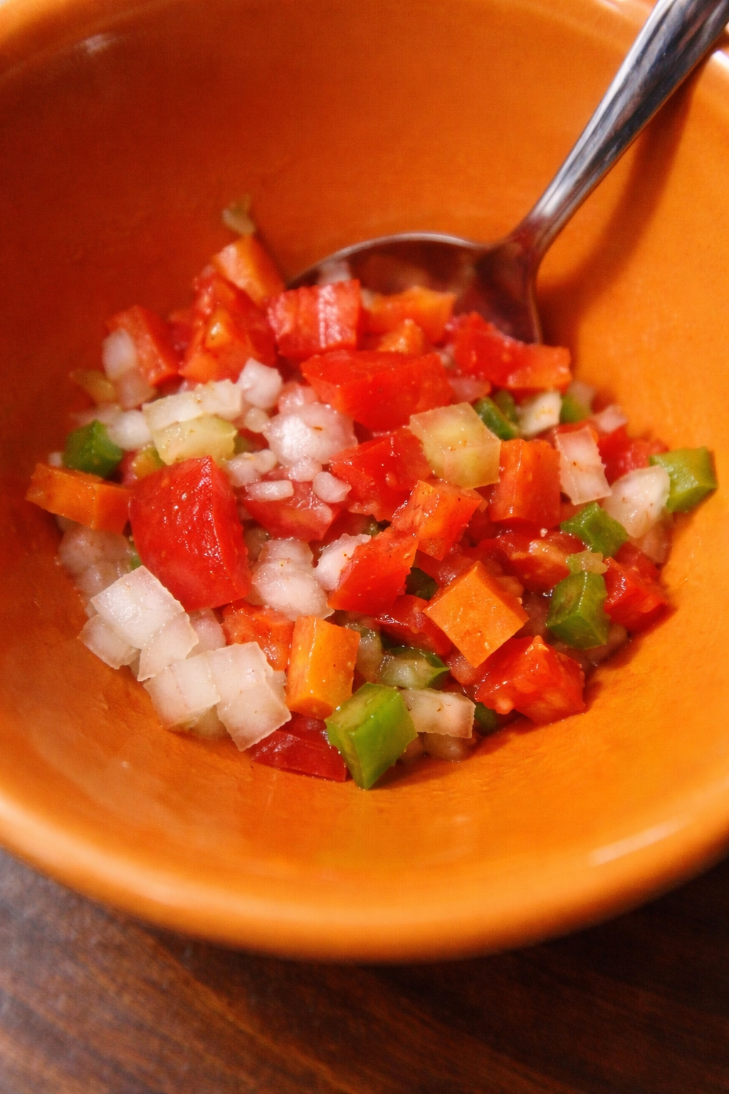 Chopped vegetables including red bell pepper, onion and green pepper mixed with seasoning in a bowl
