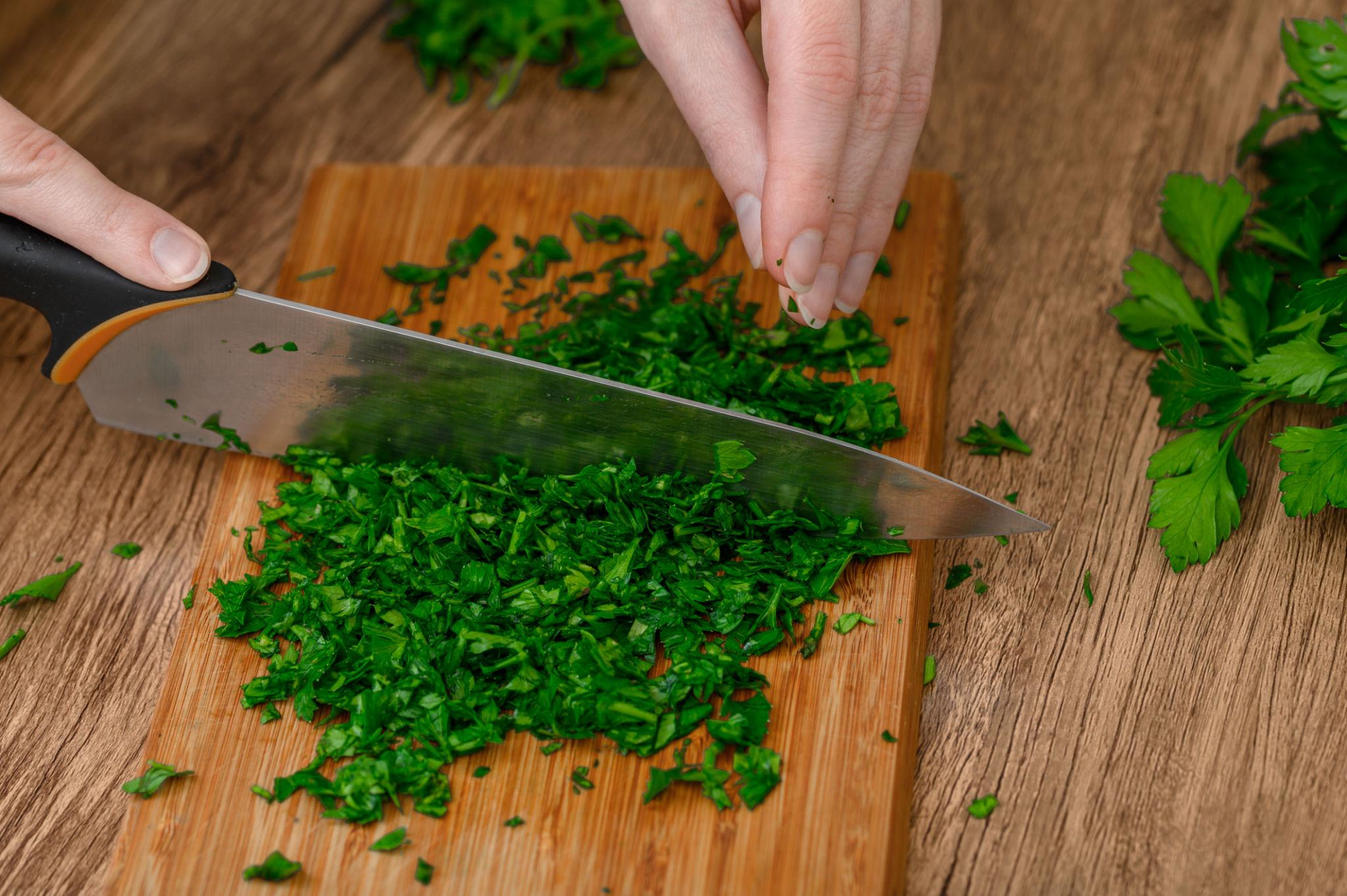 Chopping fresh parsley on a cutting board with a knife