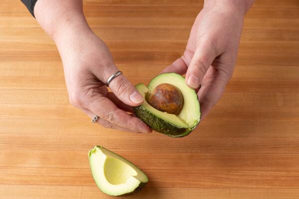 Avocado cut in half with seed being removed on a cutting board