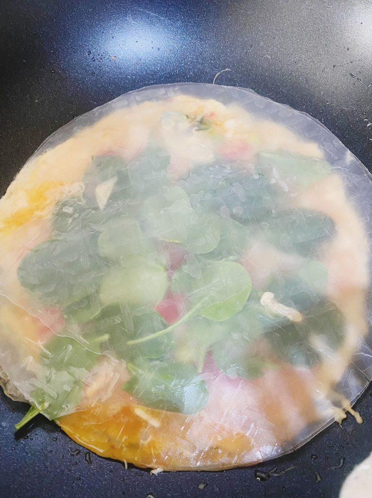 Two additional rice paper sheets placed over the cooking dish in a frying pan, forming a crispy outer layer while the ingredients cook slowly.
