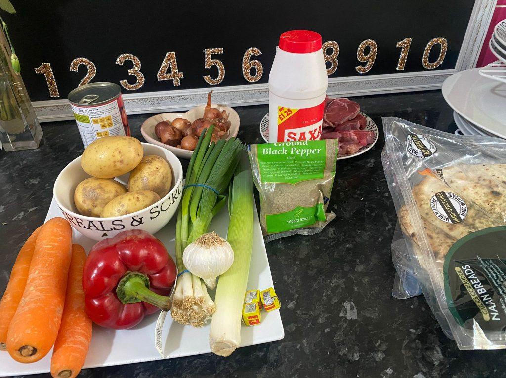 Fresh vegetables and pantry staples arranged for a hearty vegetable soup, including potatoes, carrots, leeks, garlic, and seasoning.