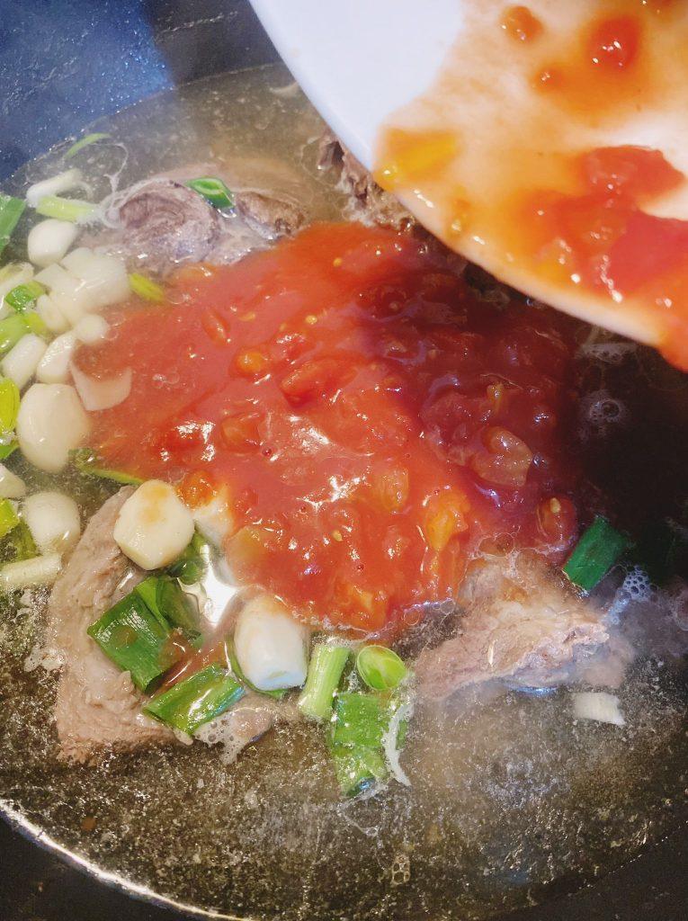 A pot of simmering vegetables with garlic, leeks, spring onions, and chopped tomatoes being added to boiling water.