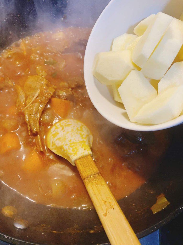Adding peeled and chopped potatoes into a simmering pot of soup with vegetables and tripe.