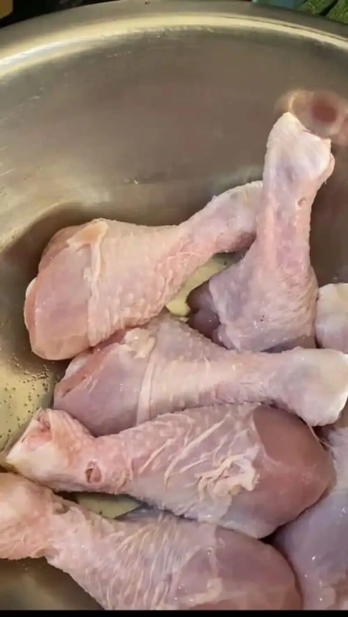 Raw chicken drumsticks placed in a large silver mixing bowl, ready for seasoning or cooking preparation.