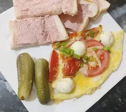 A breakfast plate with a few slices of bread topped with pâté, a cheesy omelet with roasted tomatoes, mozzarella balls, and green onions on top, with two pickles on the side—crunchy and fresh.