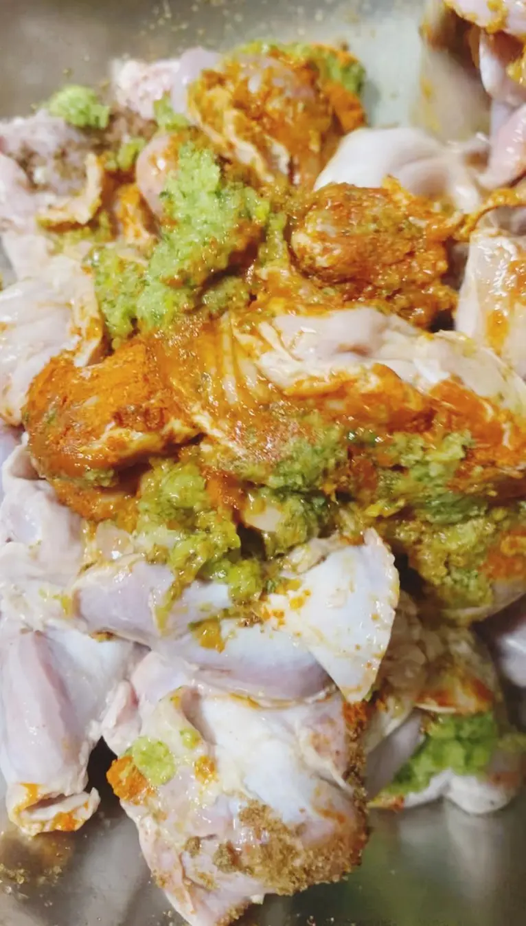 Raw chicken pieces marinated with green herb paste and orange spices in a metal bowl
