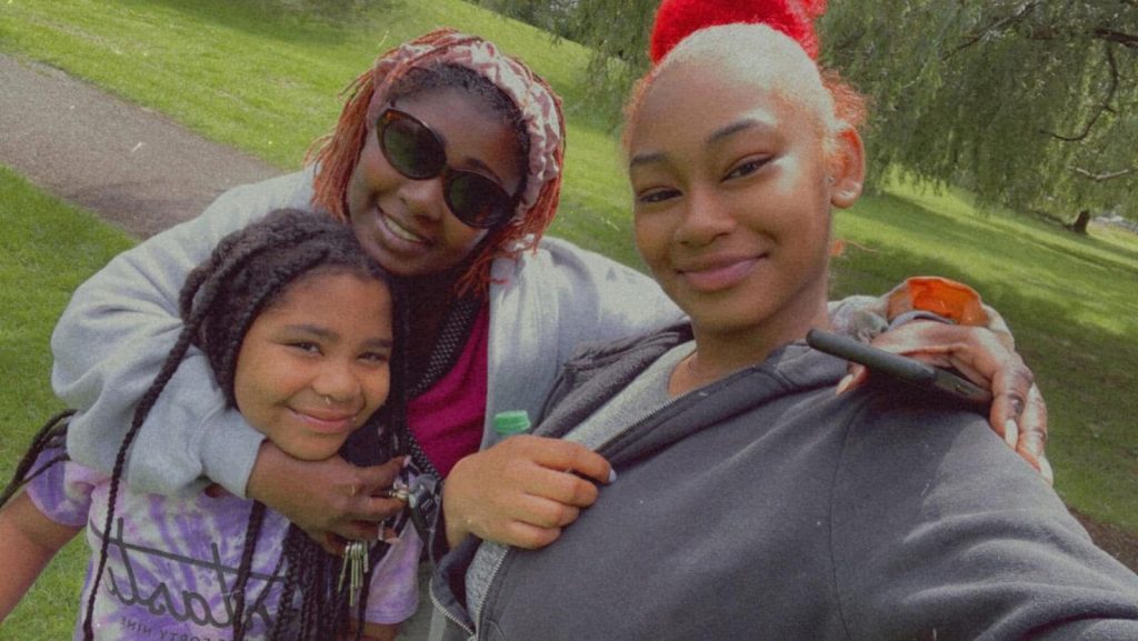 Tima smiling outdoors with her two daughters, showing the family who motivates her cooking and content creation.