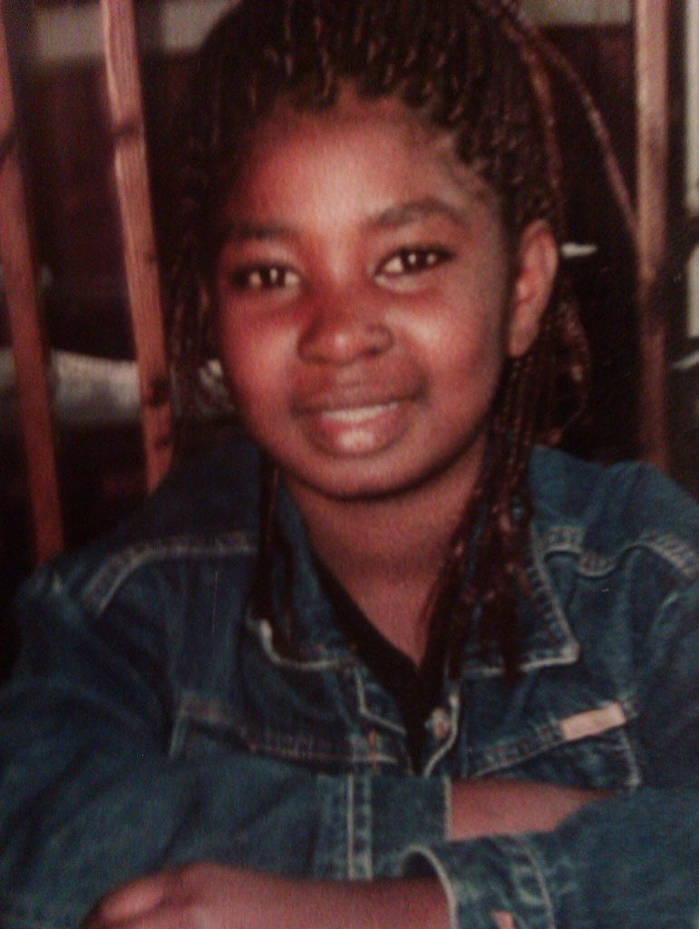 Young girl smiling in a denim jacket, representing Tima’s childhood in The Gambia where her love for cooking first began.eab52b3d