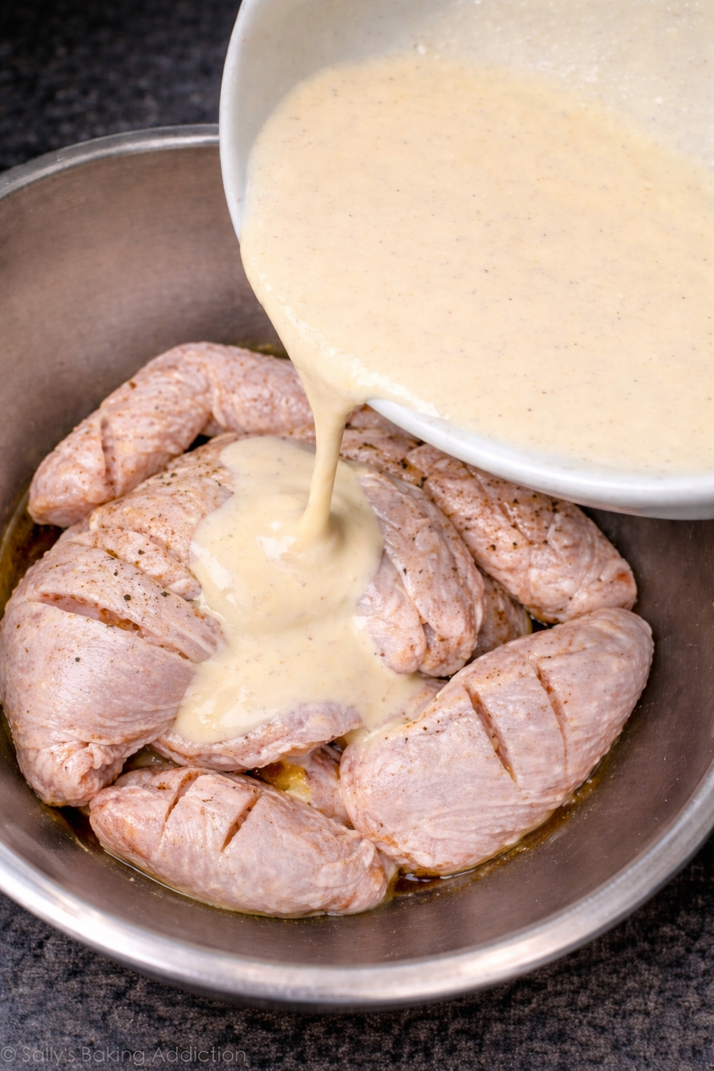 Raw chicken wings with cuts being coated with creamy marinade in a mixing bowl
