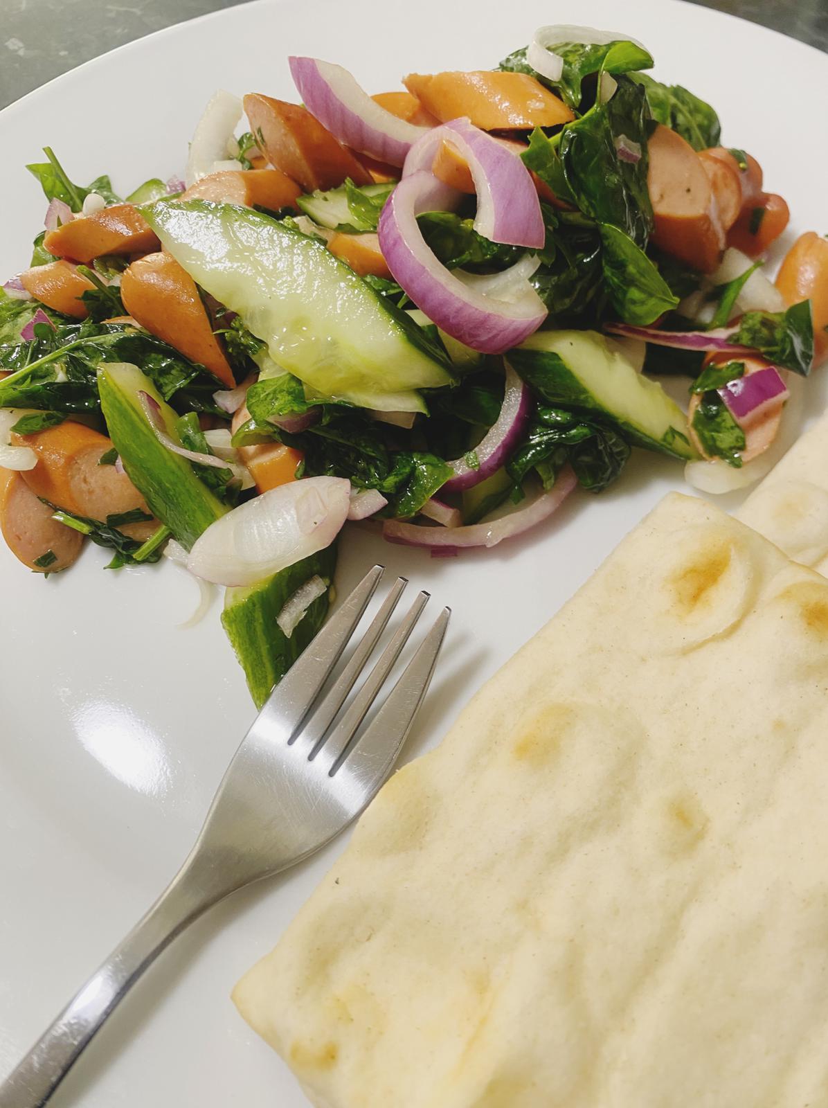 Spinach and sausage salad served on plate with bread